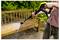 A person uses a pressure washer to clean a wooden bench in a garden, removing dirt and grime effectively.