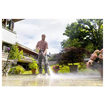 'A man using a pressure washer to clean an outdoor patio surrounded by potted plants and trees, with a building in the background.'