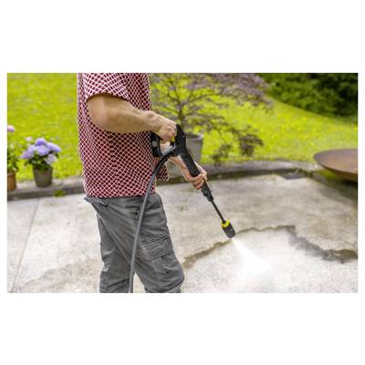 A person pressure washes an outdoor stone patio, removing dirt and grime. In the background, there is lush green grass and plants.