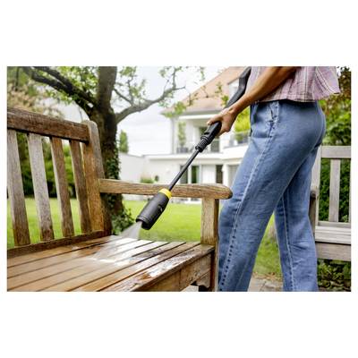 'Person cleaning a wooden bench with a pressure washer outdoors, with a house and garden in the background.'