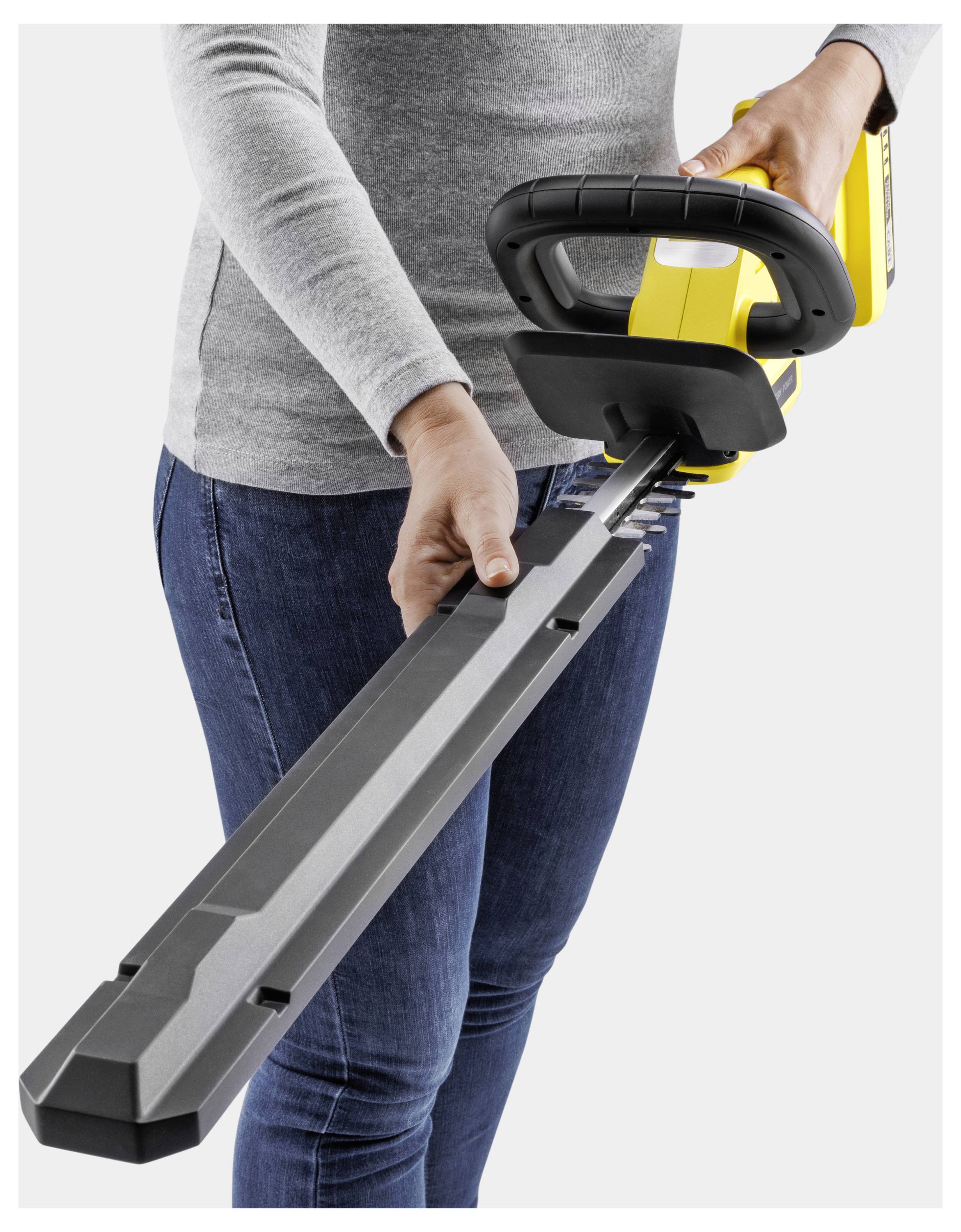 A person in jeans and a grey long-sleeve shirt holds a yellow electric leaf blower, preparing it for use.