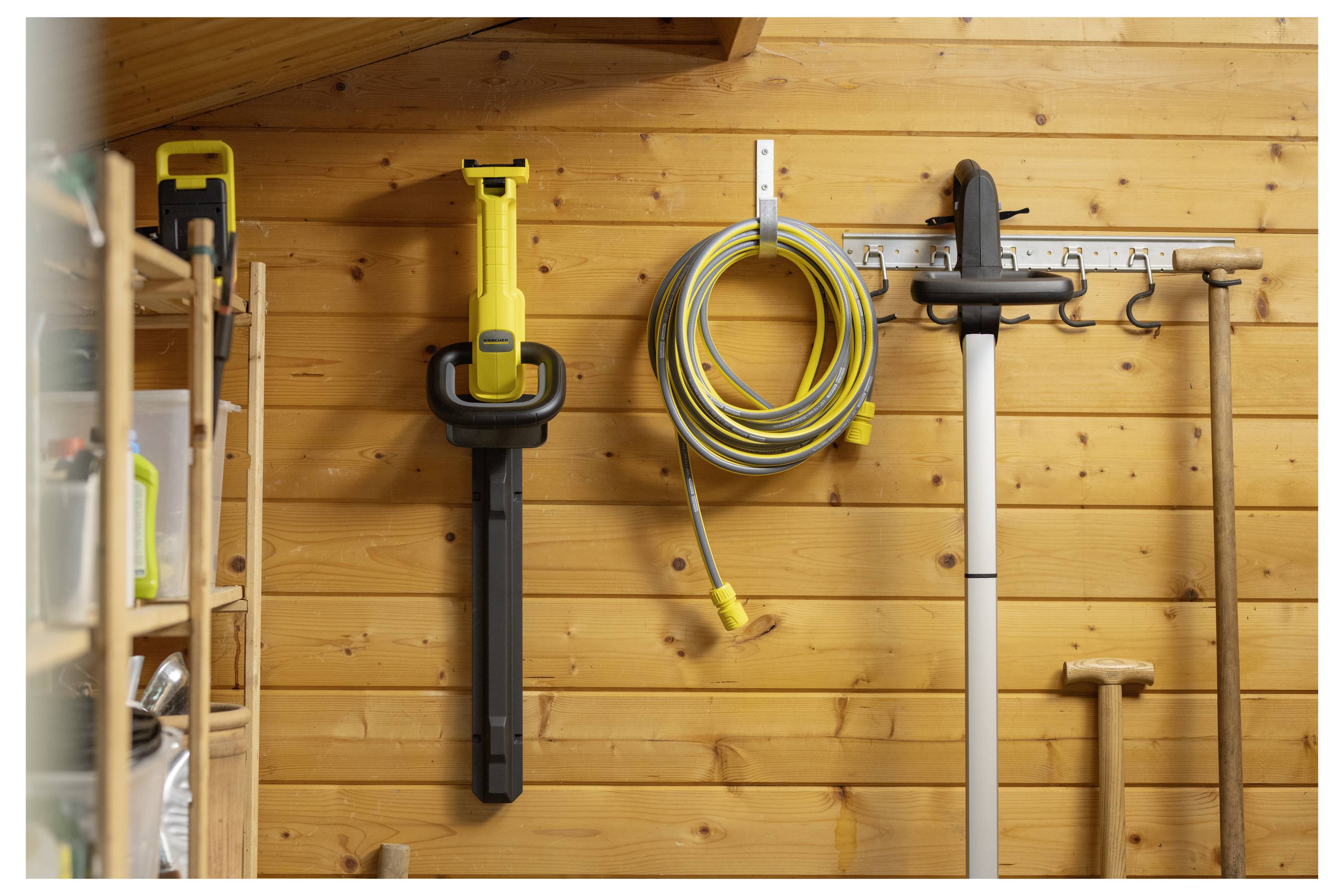 A wooden wall in a garage with a mounted yellow power tool, coiled garden hose, and various garden tools, organized and neatly hung.