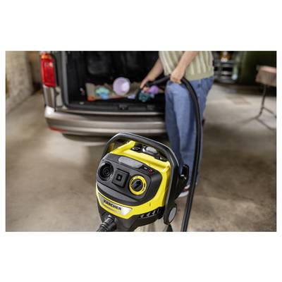 'A person vacuuming the trunk of a car with a yellow vacuum cleaner in a garage.'