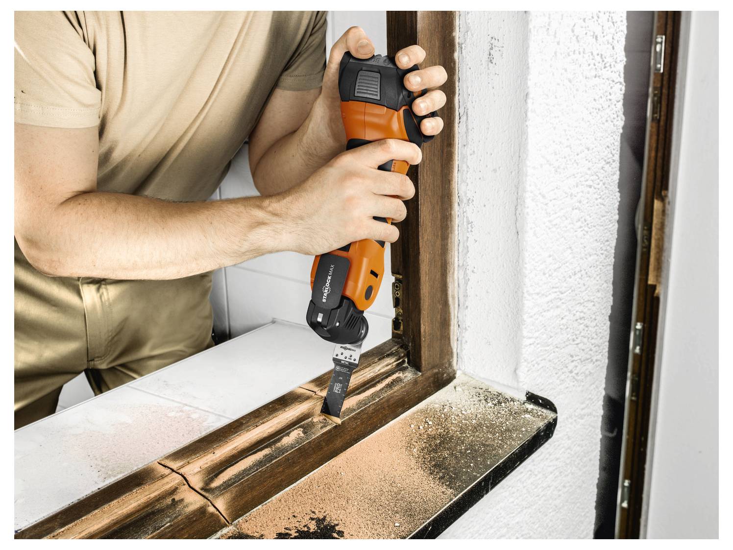 A person uses an orange power tool to sand a wooden window frame. Dust is visible on the surface.
