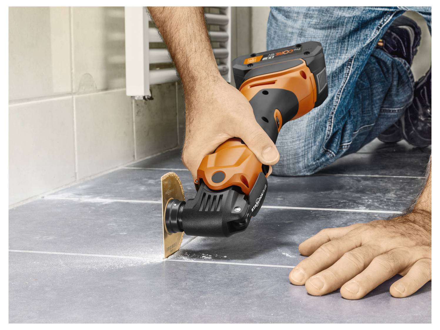 Person uses a power tool to cut grout between floor tiles. The tool is orange and black, and the person is kneeling on the floor.