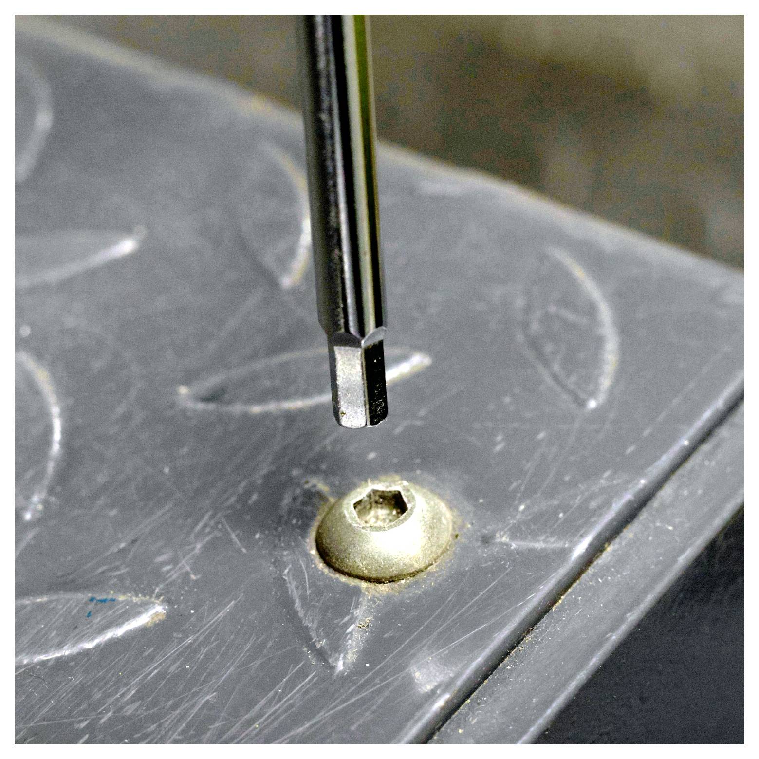 A flathead screwdriver poised above a hex socket screw on a metallic surface with a raised pattern.