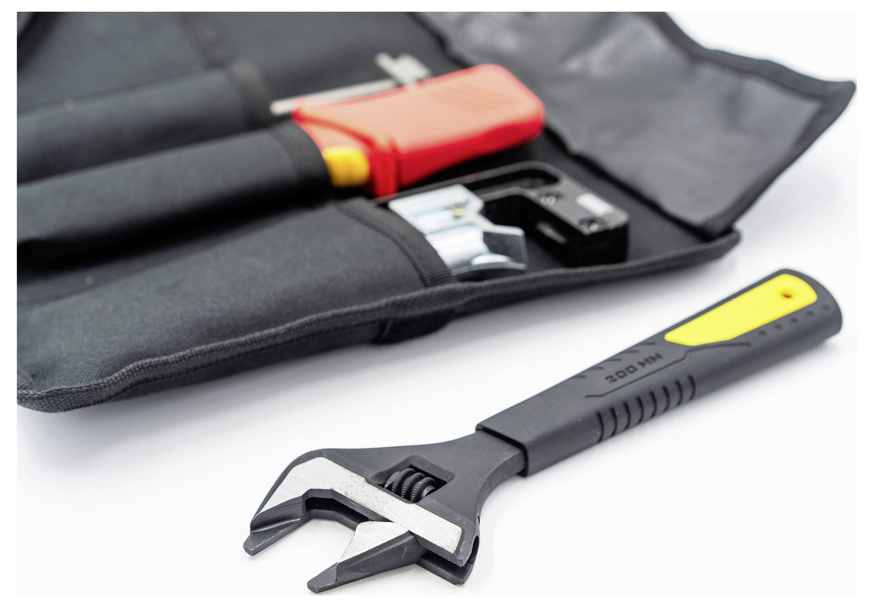 'A black and yellow adjustable wrench lies beside an open tool pouch containing a red-handled tool and other hardware, on a white surface.'