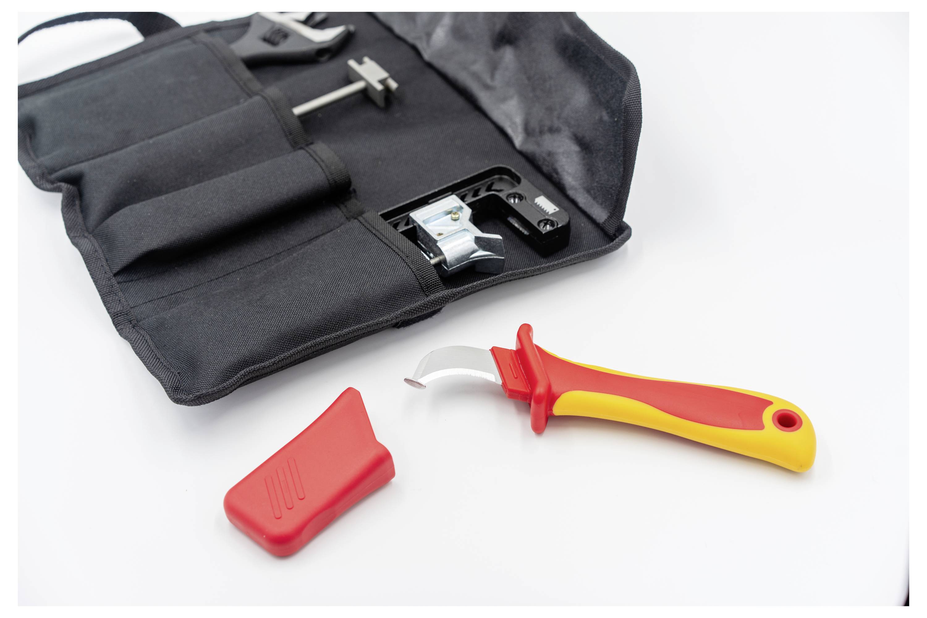 A safety can opener with a red and yellow handle is removed from its black carrying pouch, with a red cover placed beside it.