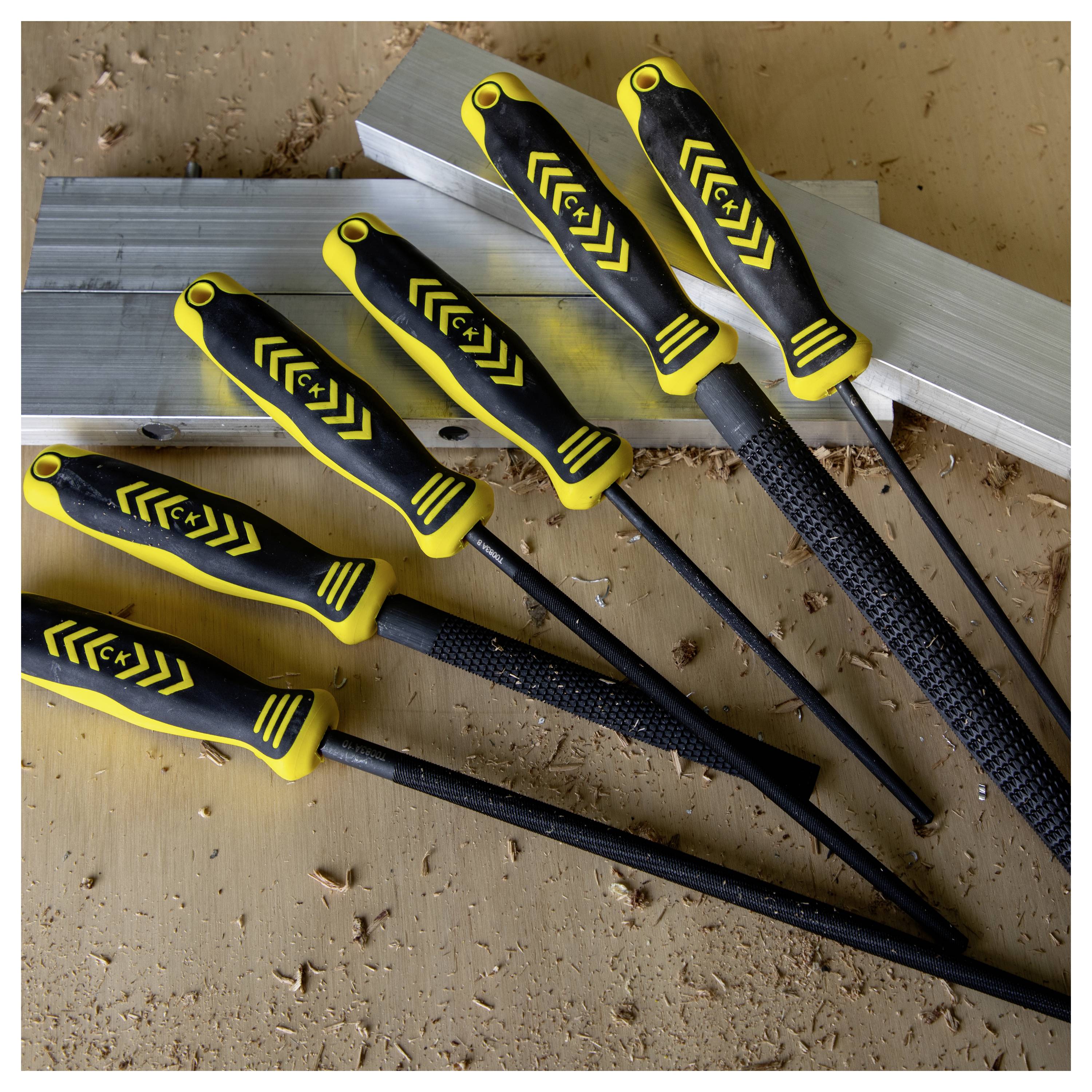 A set of six metal files with yellow and black handles displayed on a wooden surface, used for smoothing or shaping metal.