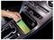 Hand places a smartphone in a car center console wireless charging tray beside cup holders and controls.<br>