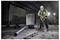 A construction worker wearing a helmet and safety vest operates a jackhammer in an unfinished building, surrounded by equipment and debris.