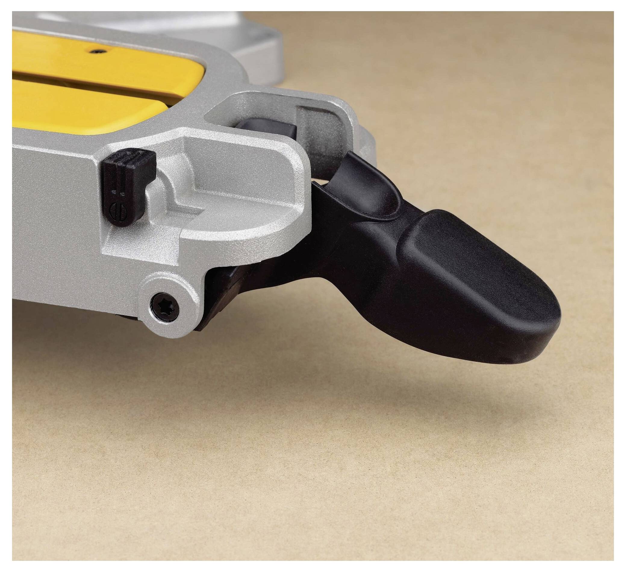 A close-up of a miter saw's adjustable lever on a beige surface, highlighting its tensioning mechanism and ergonomic handle design.