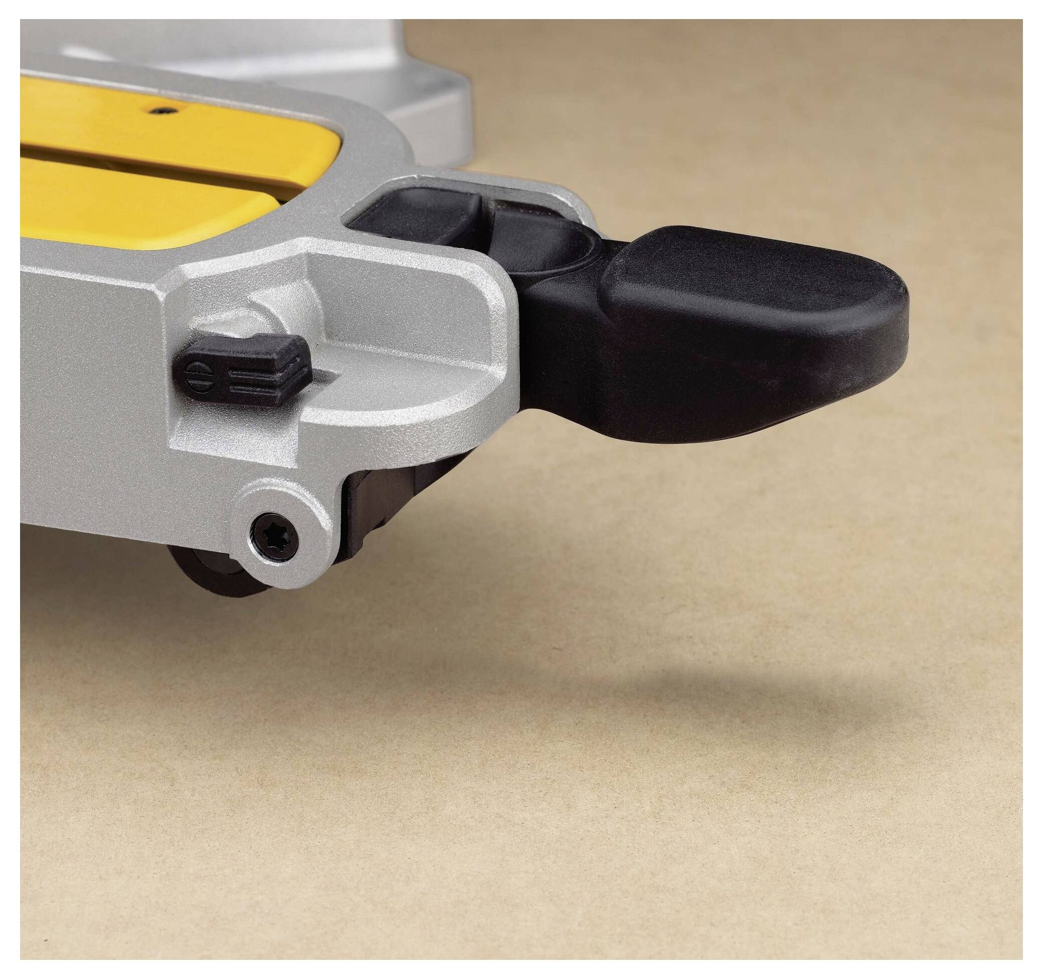 Close-up of a power tool, showing a yellow and gray body with a black component extending outward, on a textured brown background.