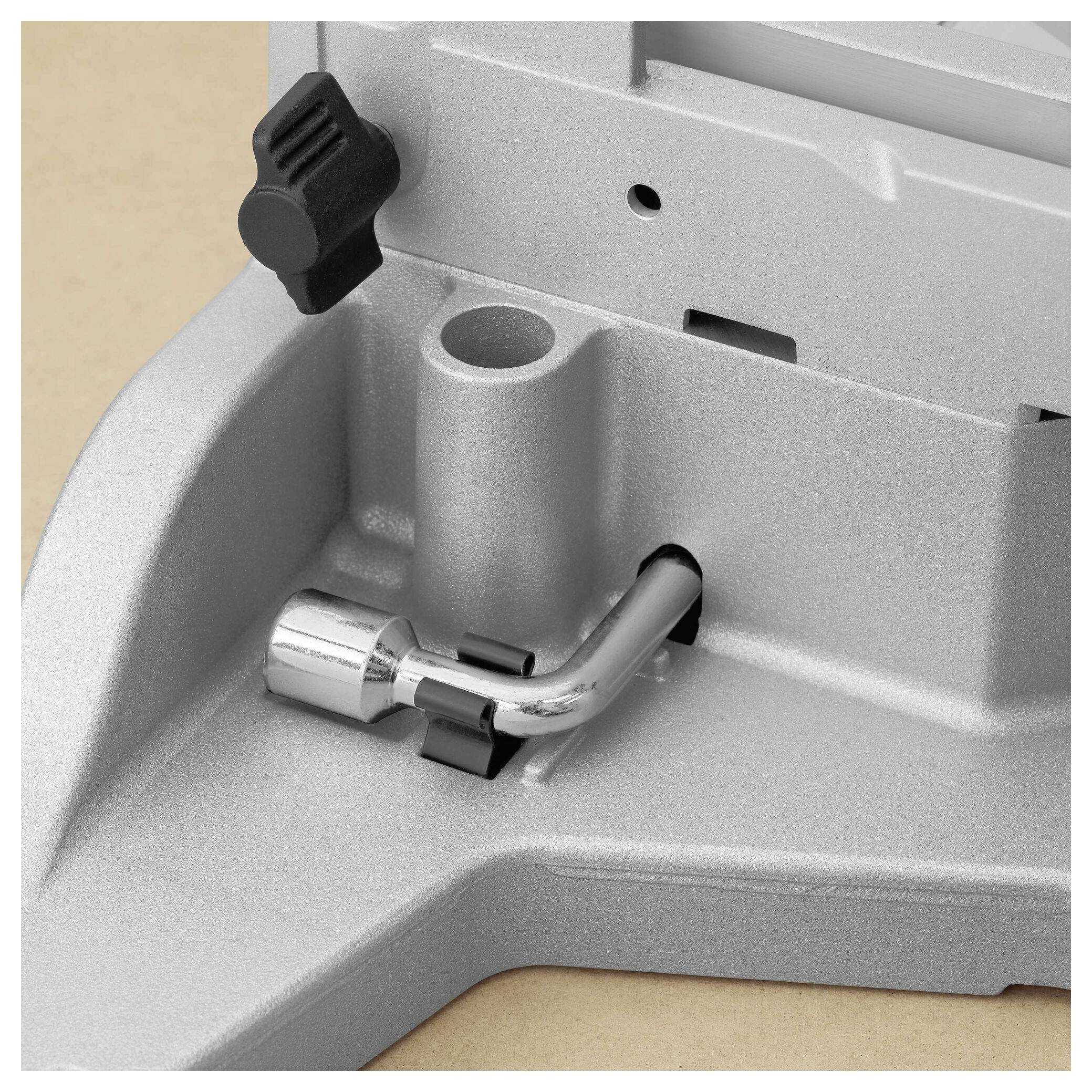 A close-up of a metallic tool component featuring a lever and adjustment knob, on a beige surface. The component suggests mechanical adjustment.