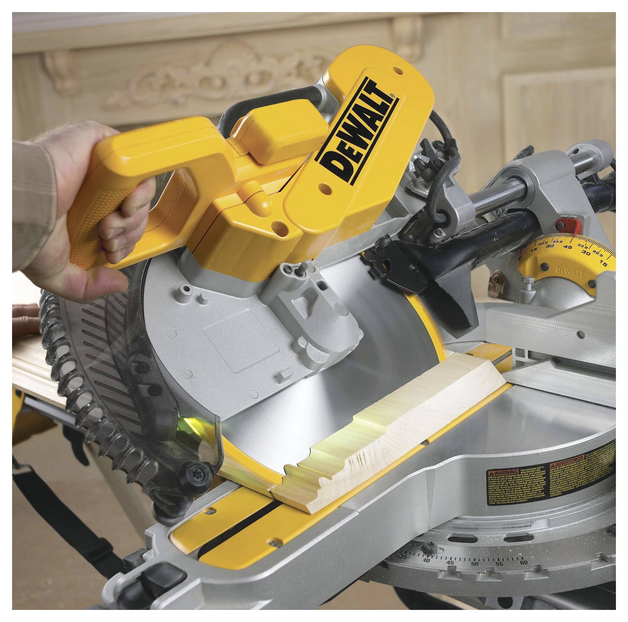 A person uses a yellow miter saw to cut a piece of wood. The saw handle is visibly marked with the brand name in black lettering.