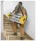 A person in brown overalls carries a folded yellow ladder up a staircase, illustrating ease of transport for the compact ladder design.
