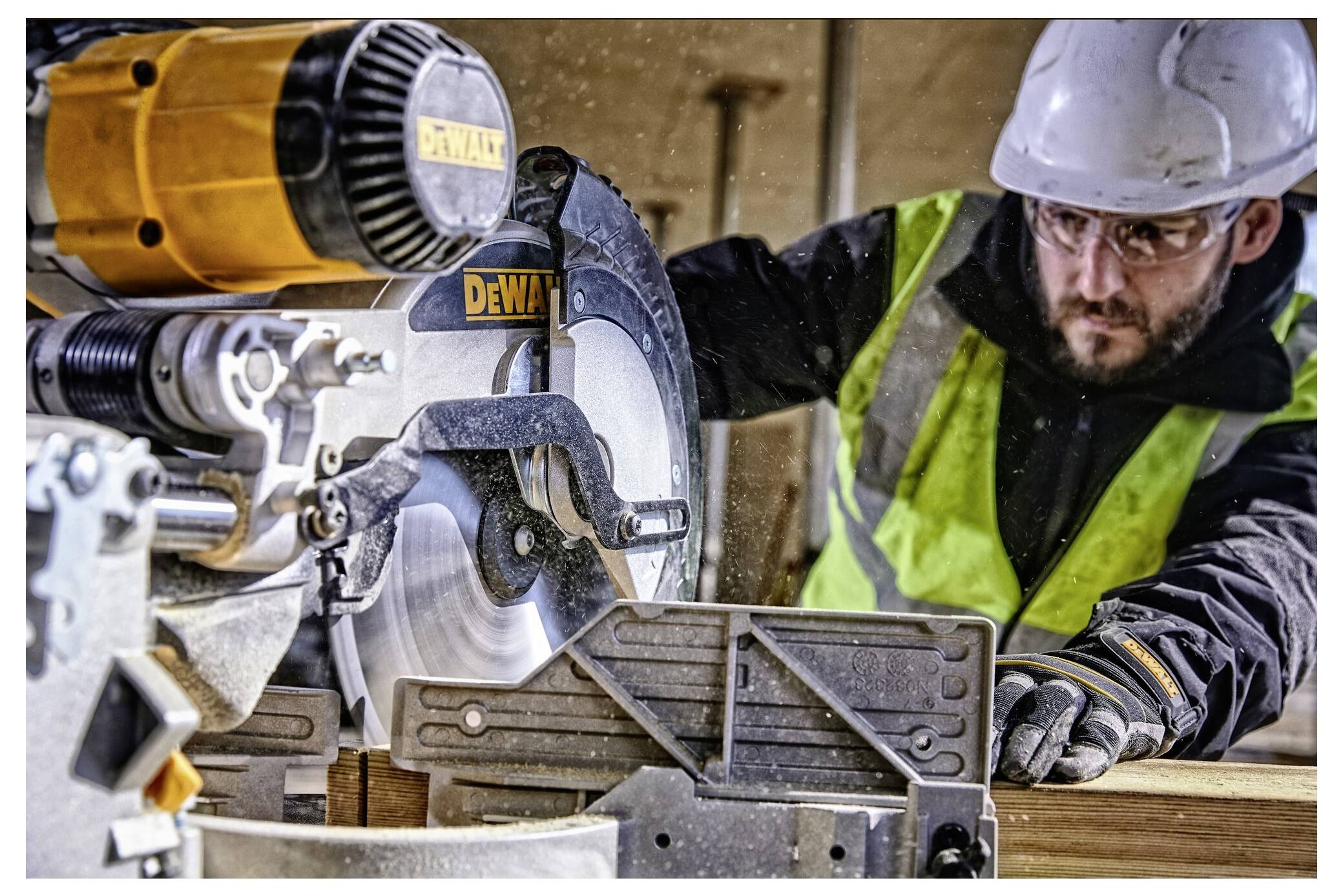 A construction worker wearing safety gear operates a circular saw, cutting wood inside a workshop.