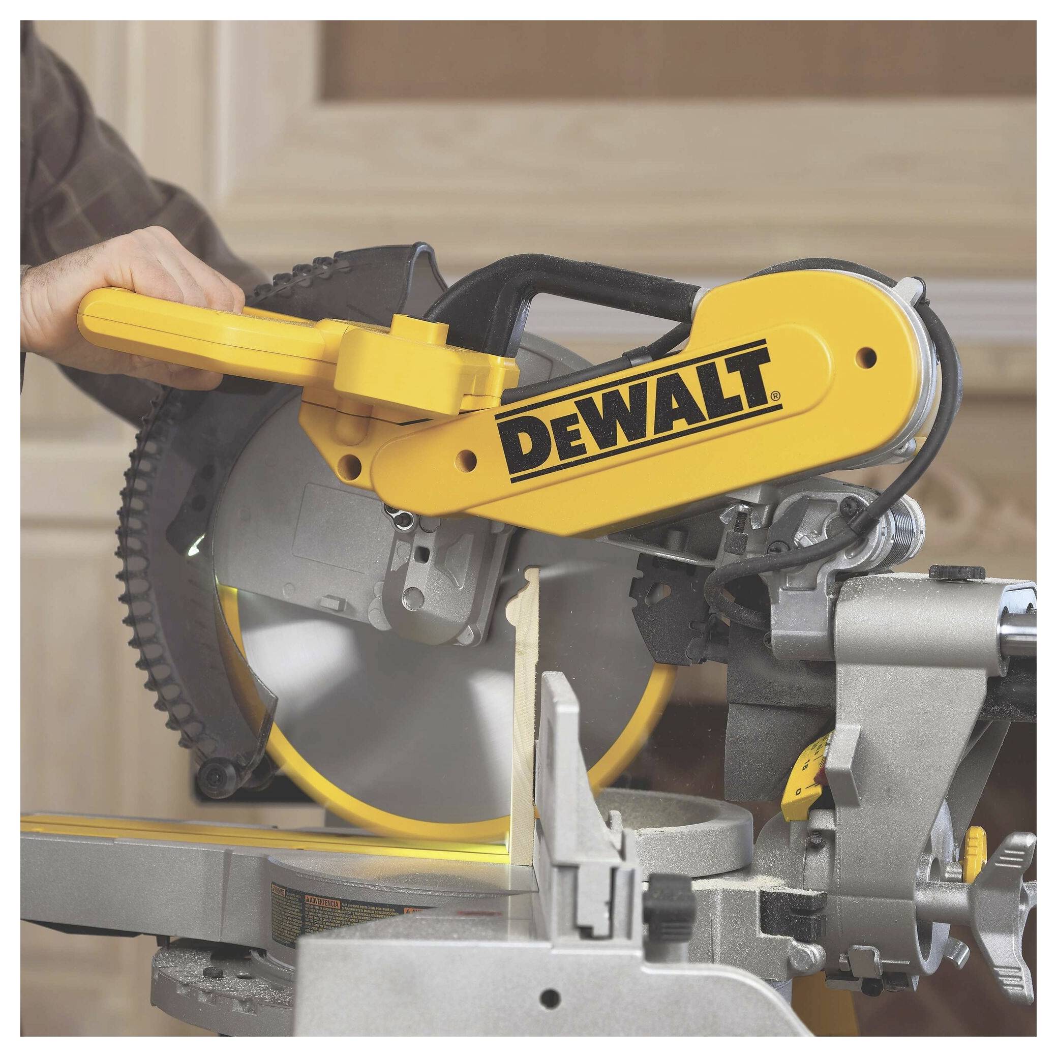 A person using a yellow DeWalt miter saw to cut wood in a workshop.