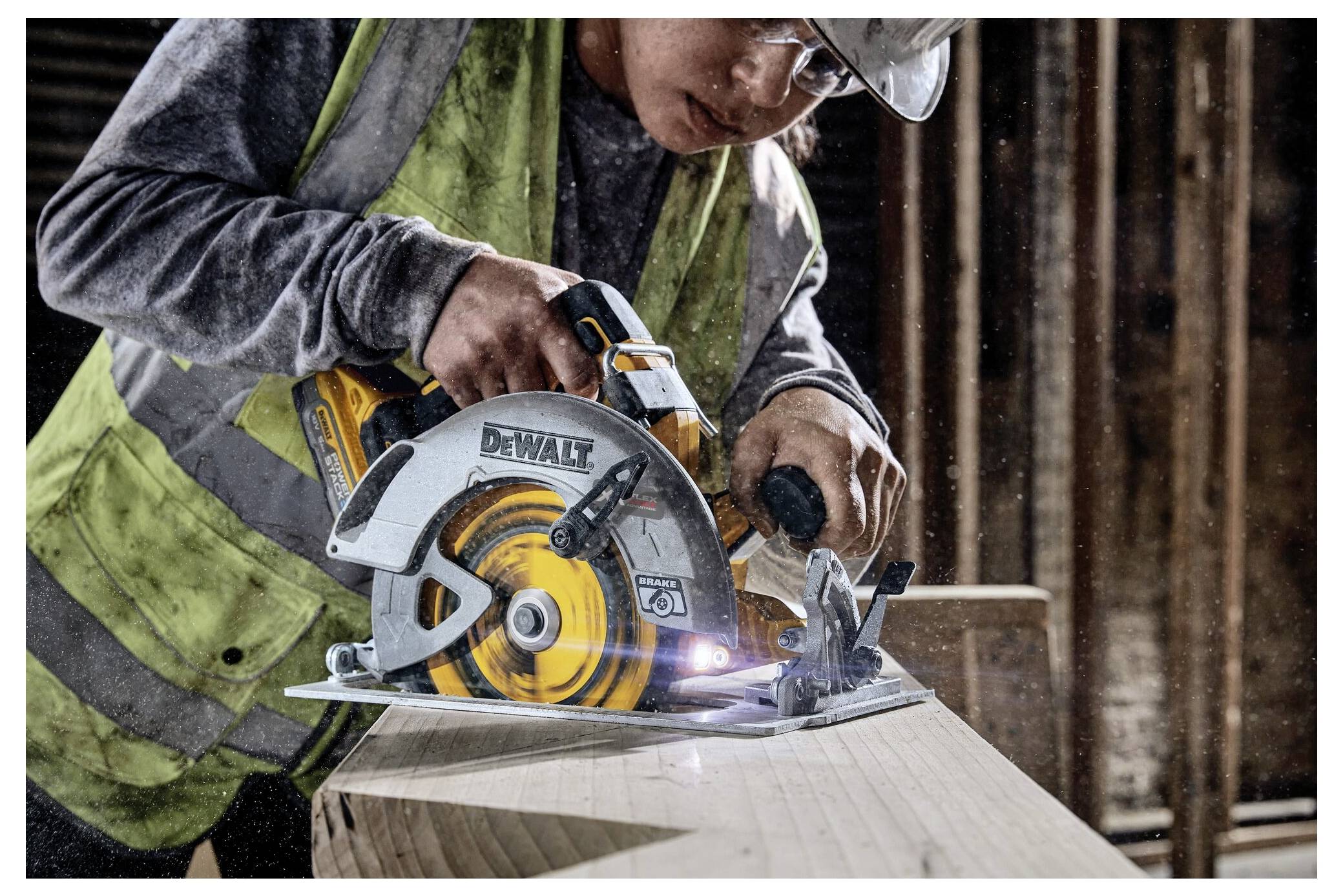 A worker in protective gear uses a circular saw to cut wood, with sawdust in the air, highlighting a construction environment.