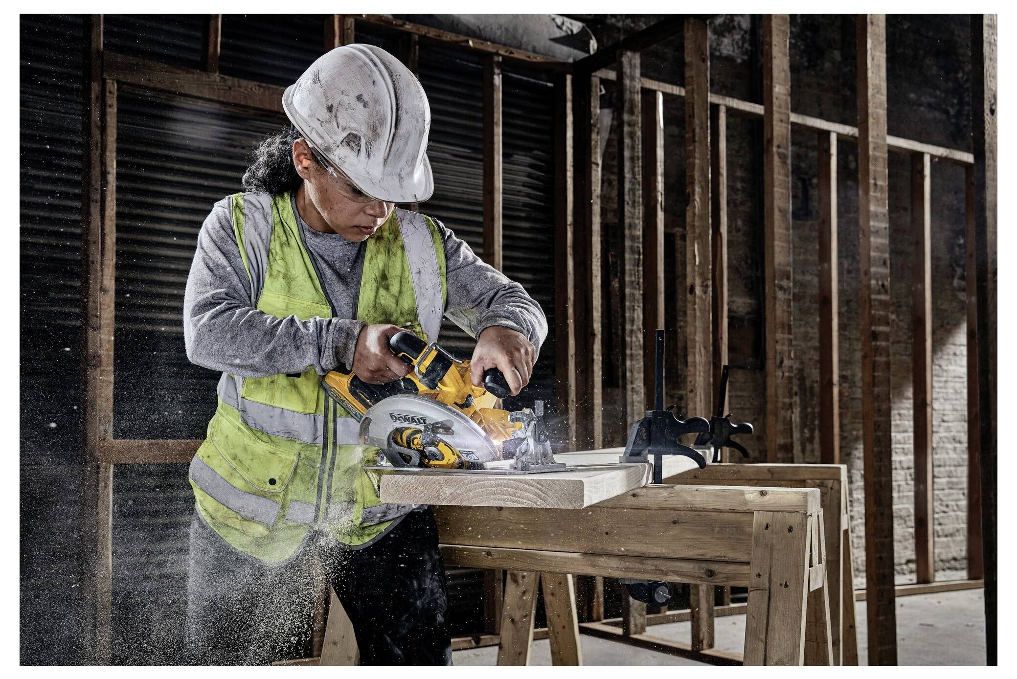 A construction worker in safety gear uses a circular saw on wood in a partially constructed building.