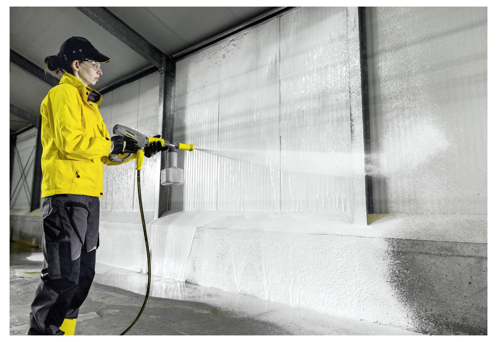 A person in protective gear uses a power washer to clean the interior wall of a large industrial facility.