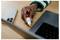Hand holding a small USB-C adapter beside a laptop and smartphone on a desk.