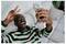 Smiling man on a couch takes a selfie with his phone, flashing a peace sign.<br>