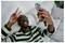 Smiling man lying on a bed takes a selfie with his smartphone while making a peace sign.<br>