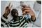 Smiling man in a striped shirt taking a selfie and flashing a peace sign with a smartphone.<br>