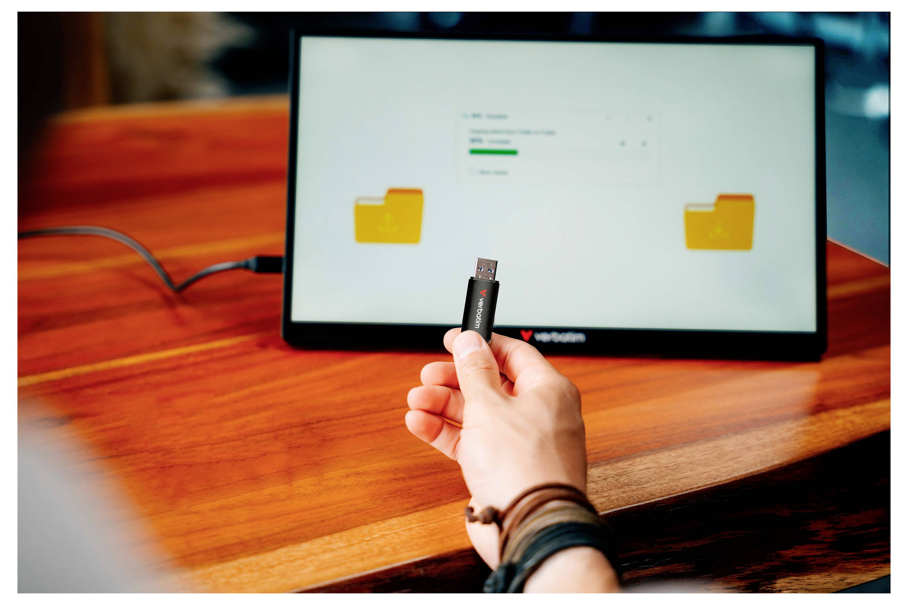 Hand inserts a USB flash drive toward a laptop screen showing folder icons, suggesting file transfer or device connection.