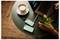 Overhead view of a laptop workspace with a coffee cup, phone cases, pen, and a hand holding a mint drink on a round table.