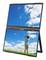 Portable dual-screen monitor showing one display with blue sky and clouds and the other with a child standing in a grassy field looking up.