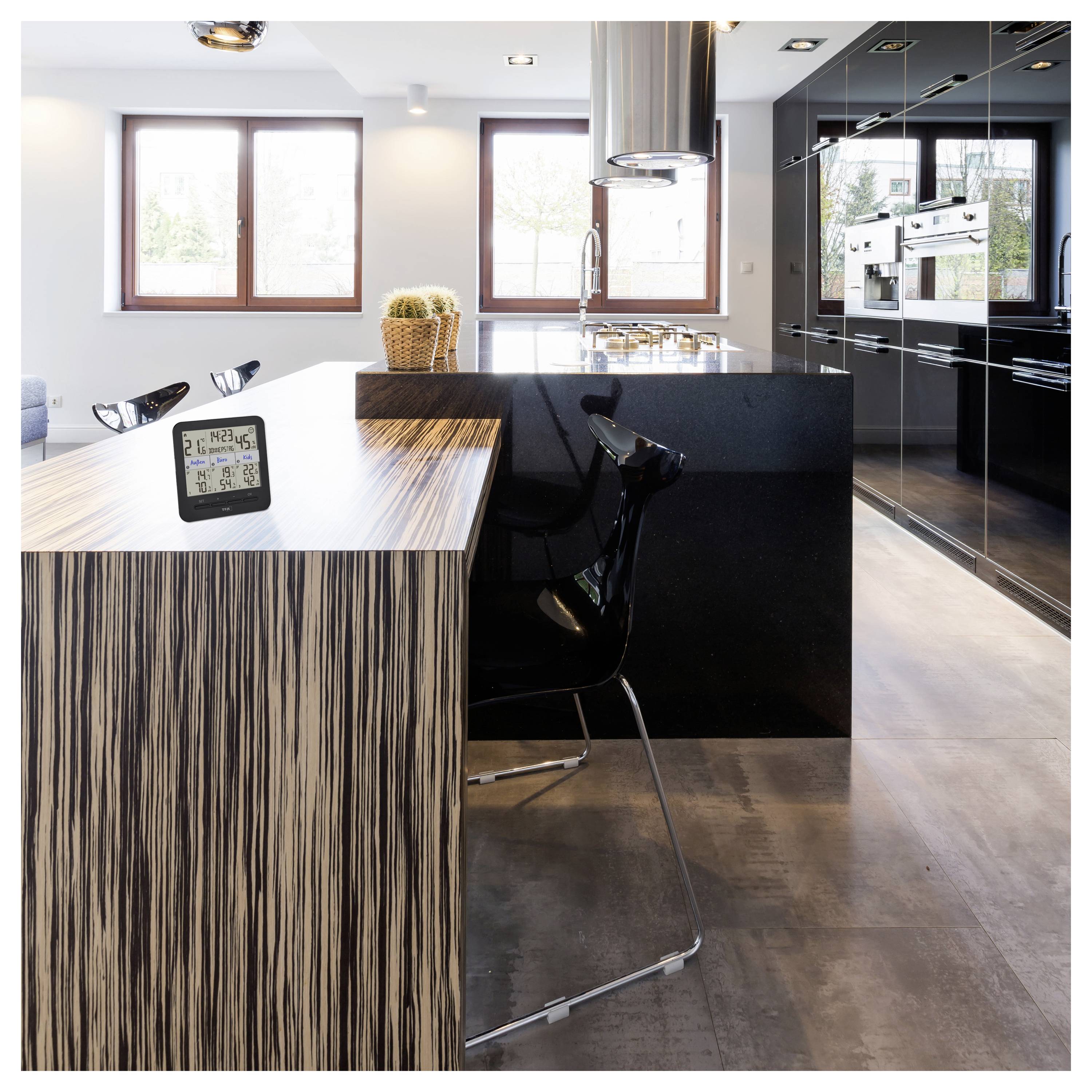 A modern kitchen with a wood-patterned island and black bar stool. A digital clock displays time and date. Large windows provide natural light.