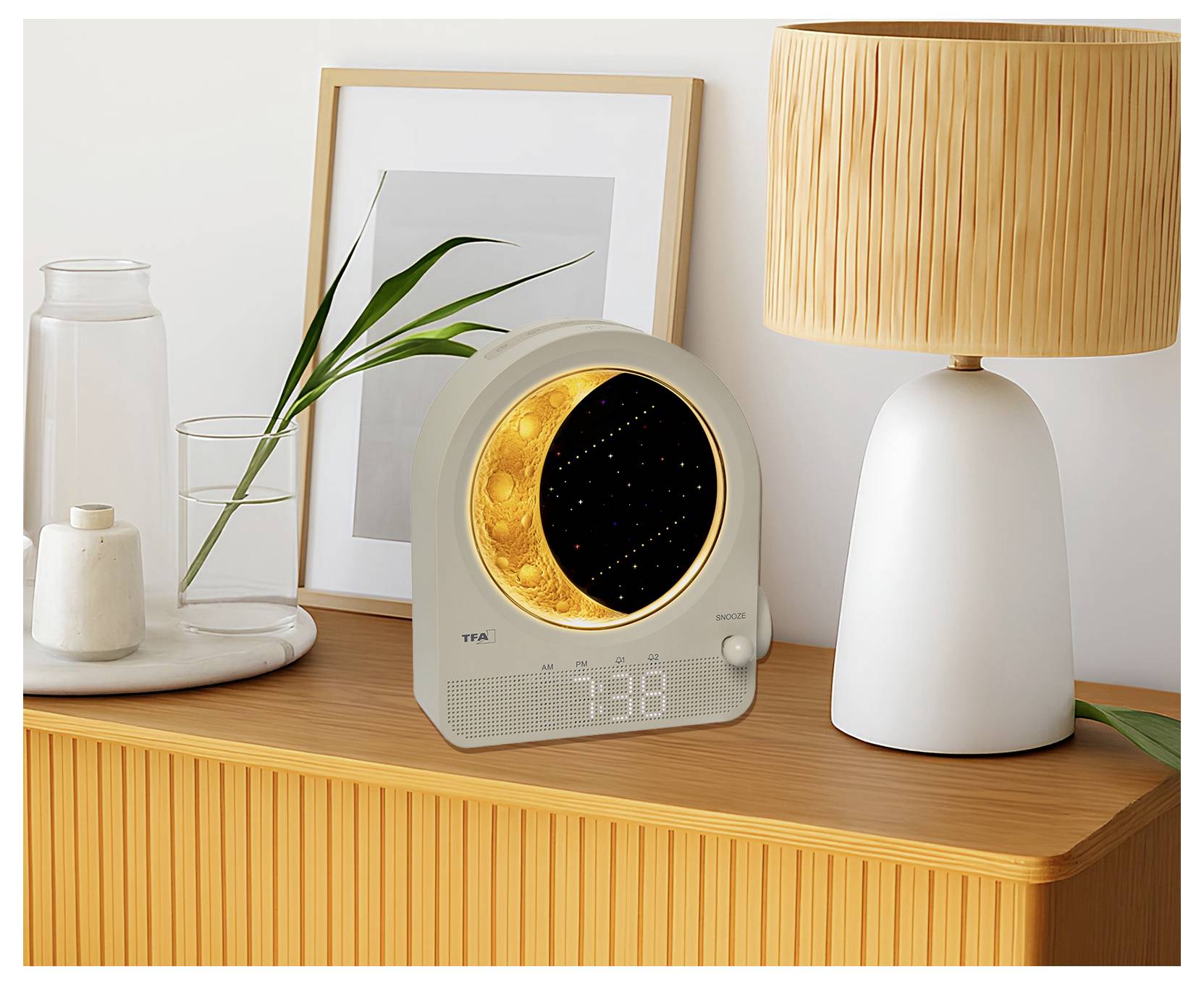 A round digital clock with a nature-themed night light on a wooden cabinet beside a lamp and framed picture. Time displayed: 7:38.