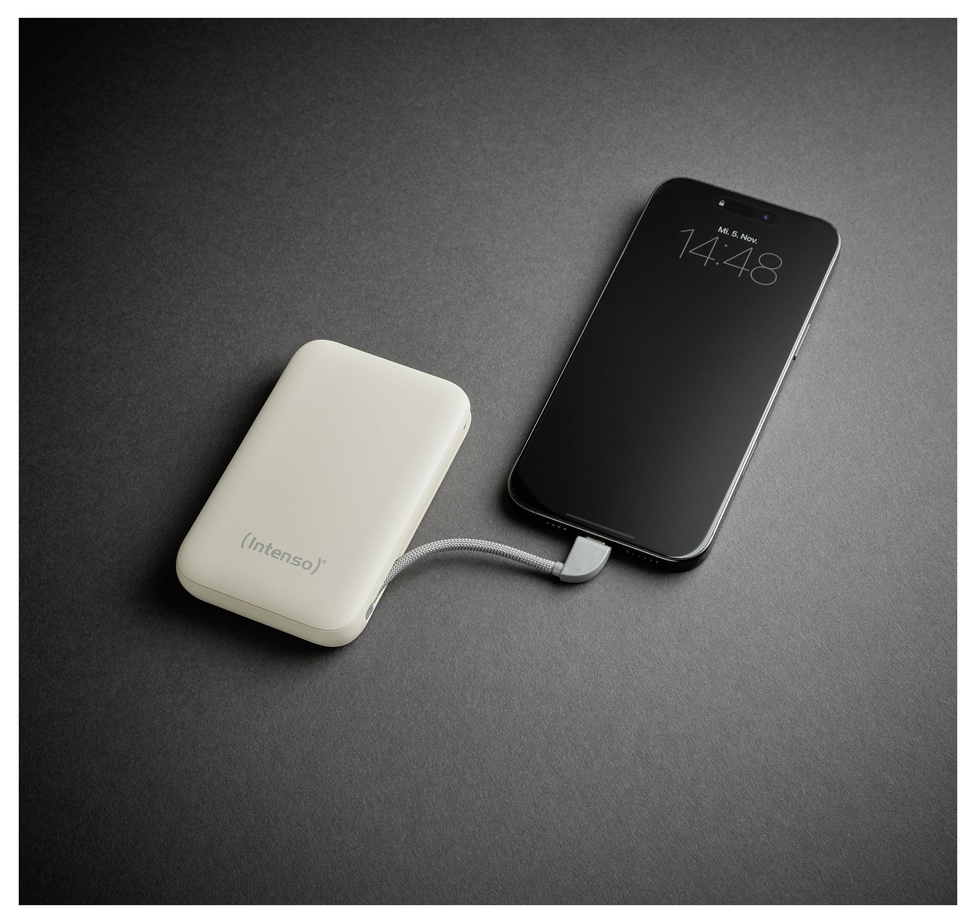 A smartphone connected to a portable power bank with a cable, resting on a dark surface. The phone screen displays the time, 14:48.