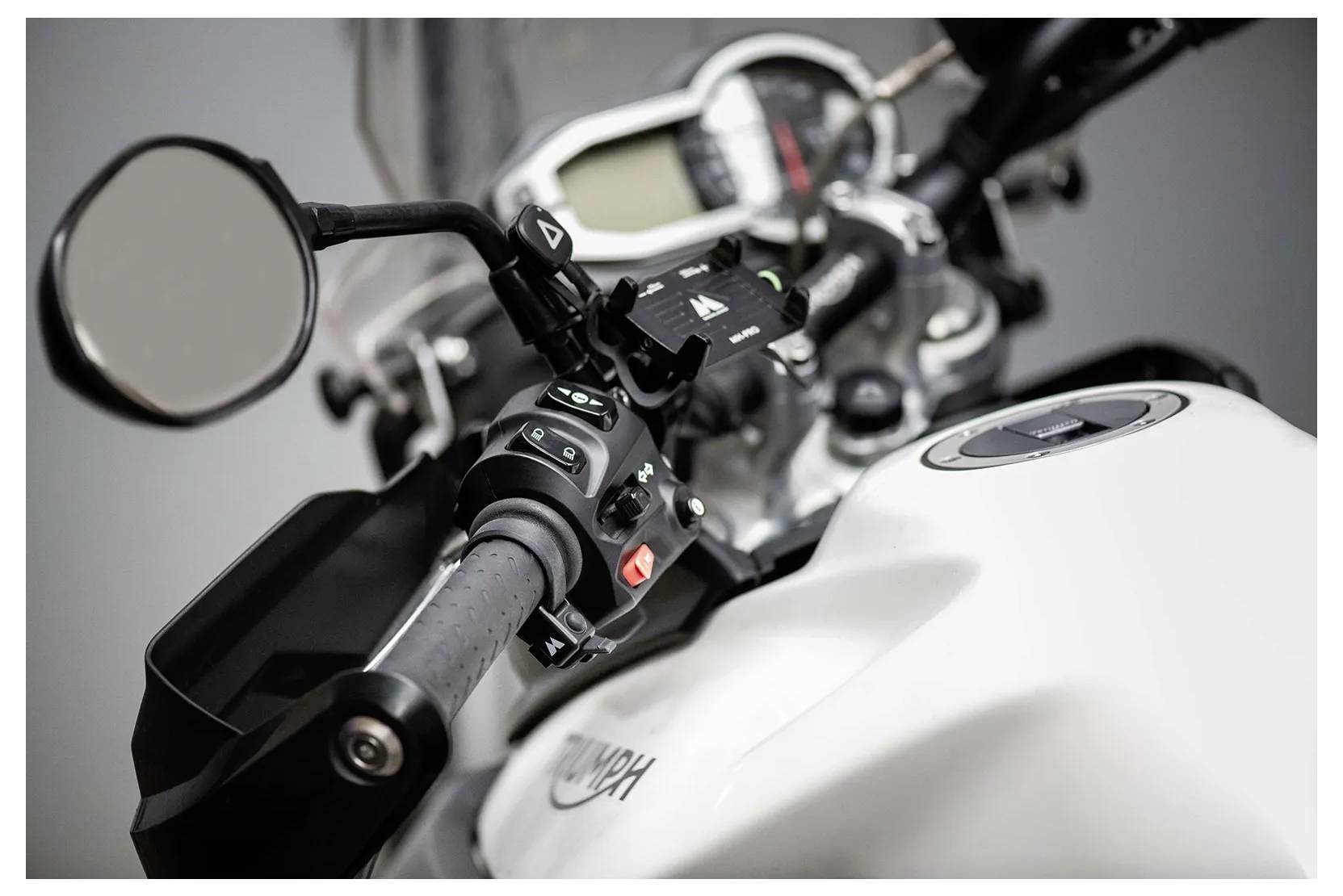Close-up view of a motorcycle's handlebar and control panel, highlighting the speedometer, mirror, and control switches.