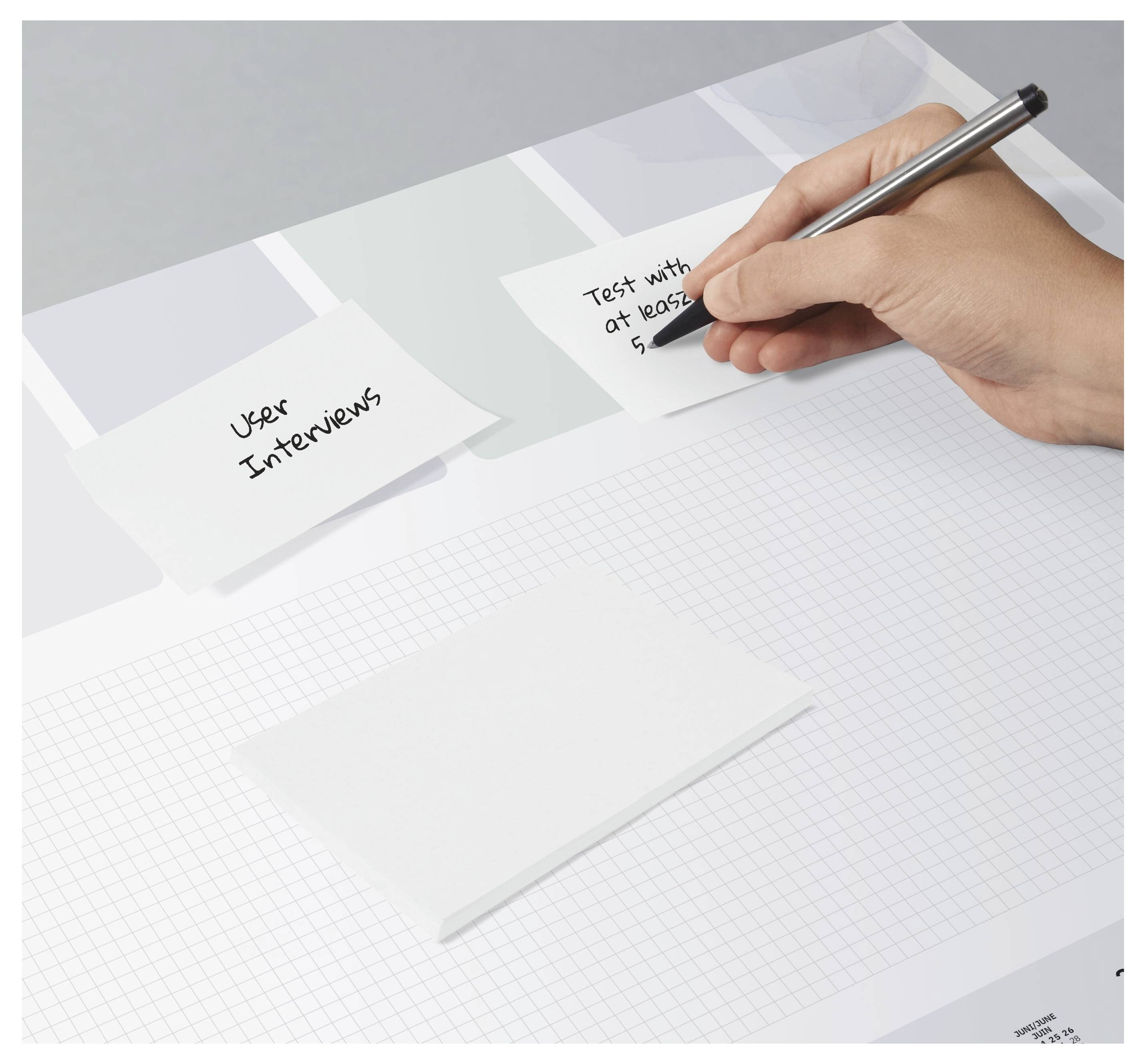 'A person writes on a sticky note with a pen in hand. Another note reads 'User Interviews'.'