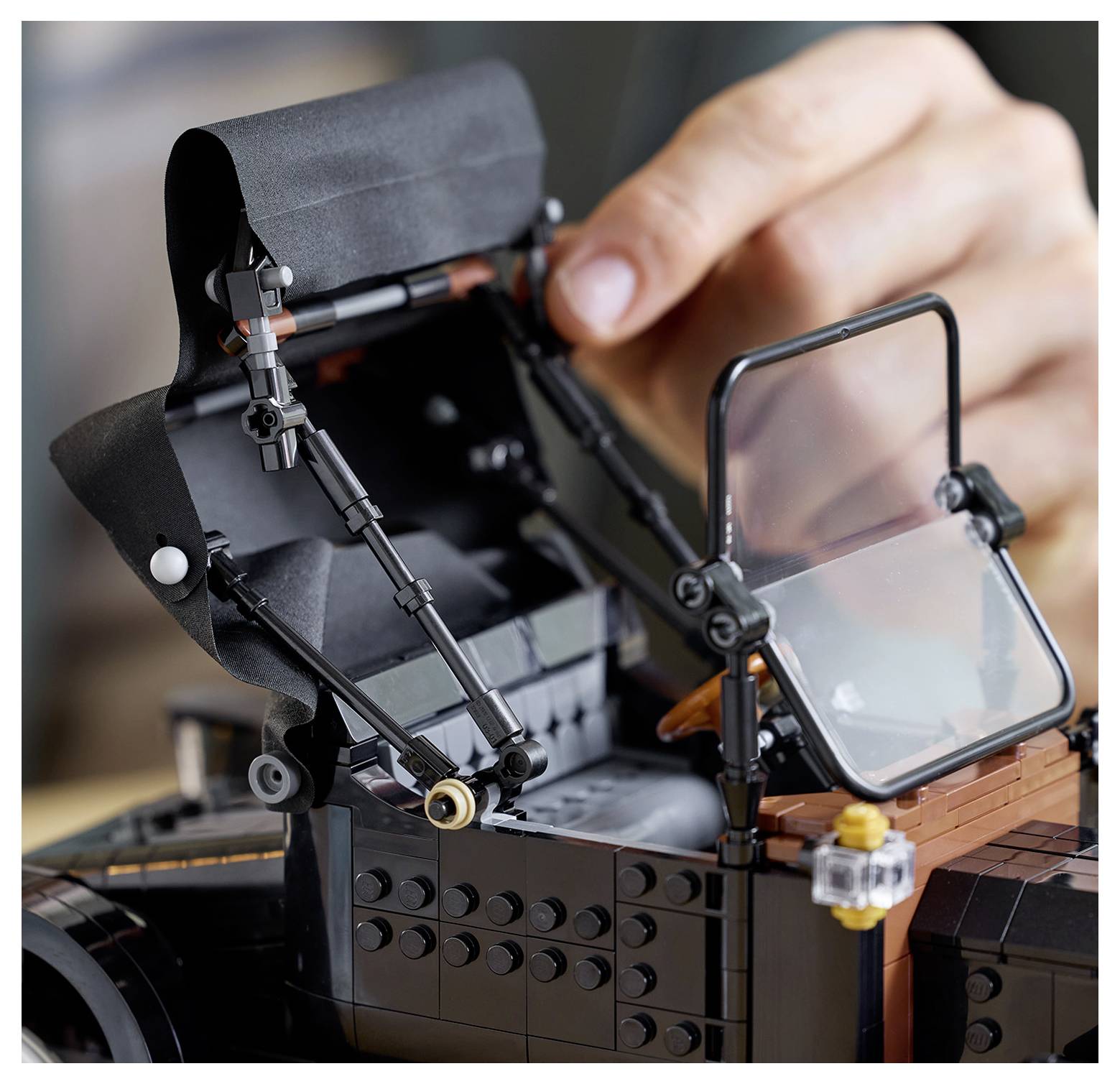 'A close-up of a hand opening the canopy of a detailed LEGO model of a classic sports car, showcasing intricate assembly and design.'