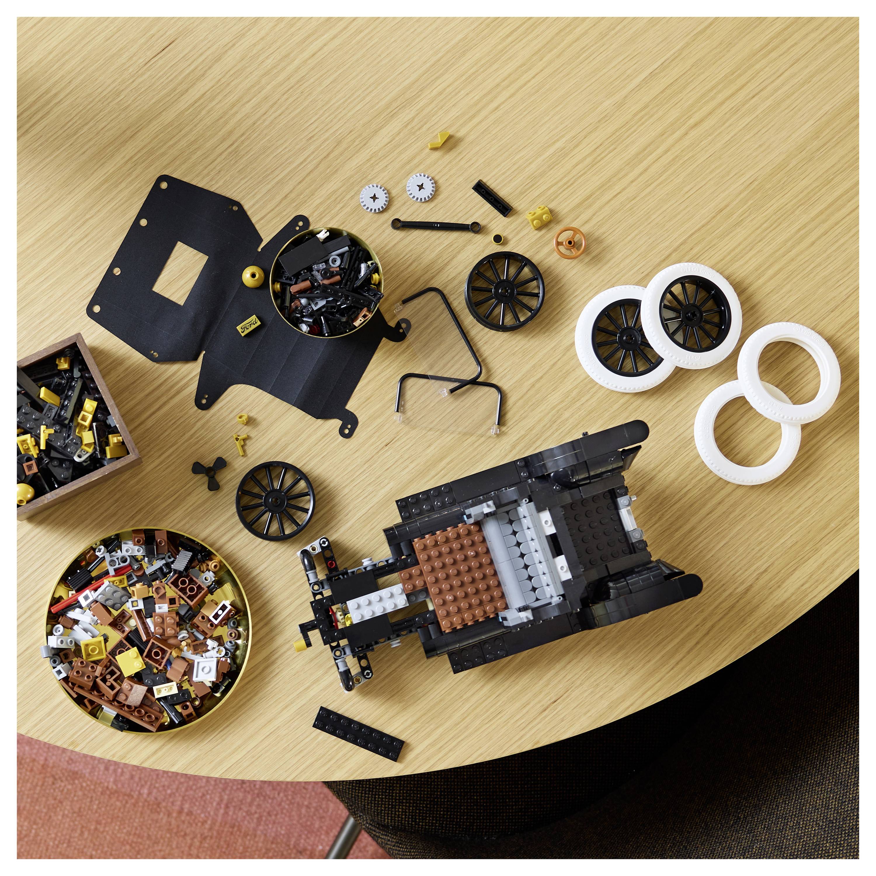 'Lego pieces and partially assembled vehicle on a wooden table, including wheels, gears, and various small blocks.'
