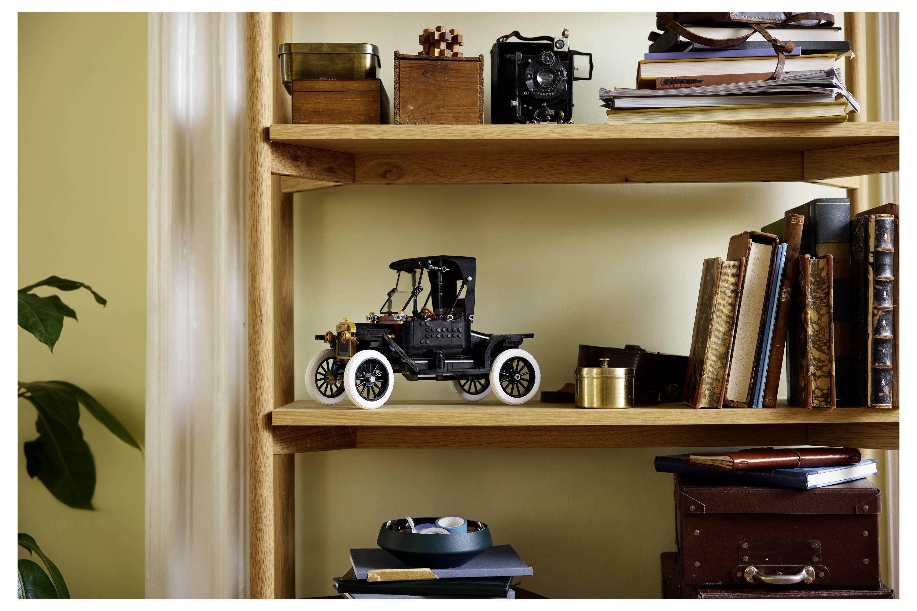 A wooden bookshelf with decorative items: a model vintage car, books, a vintage camera, and assorted office supplies neatly arranged.