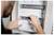Person installs or adjusts a white wall-mounted electrical panel, aligning metal rails with both hands.<br>
