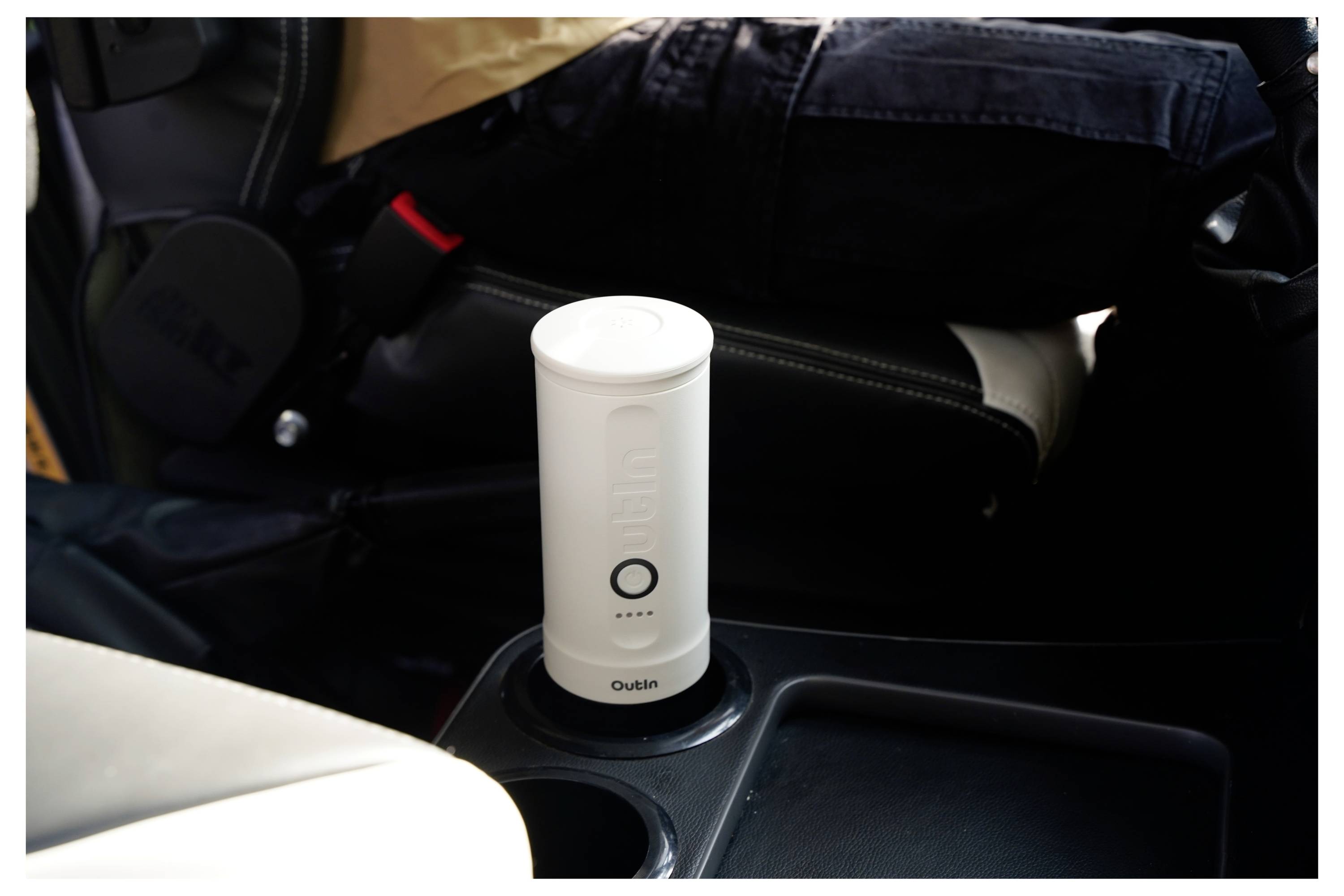 A portable air purifier in a car's cup holder, designed for on-the-go purification, is powered on and displaying four illuminated dots.