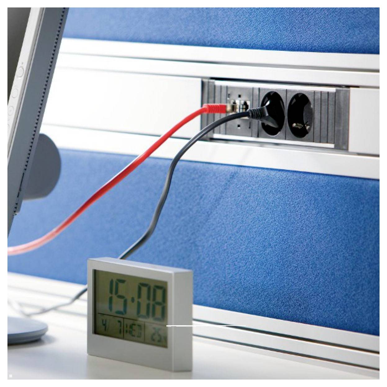 A power strip with multiple outlets is attached to a wall above a digital clock displaying '15:08'. Cables are connected to the strip.