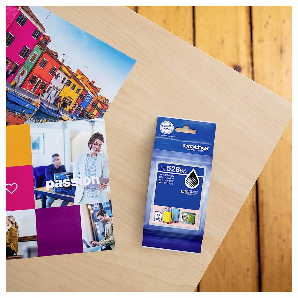 A colorful ink cartridge packaging labeled 'brother LC-528BK' on a wooden table next to vibrant photo print samples showcasing vivid colors.