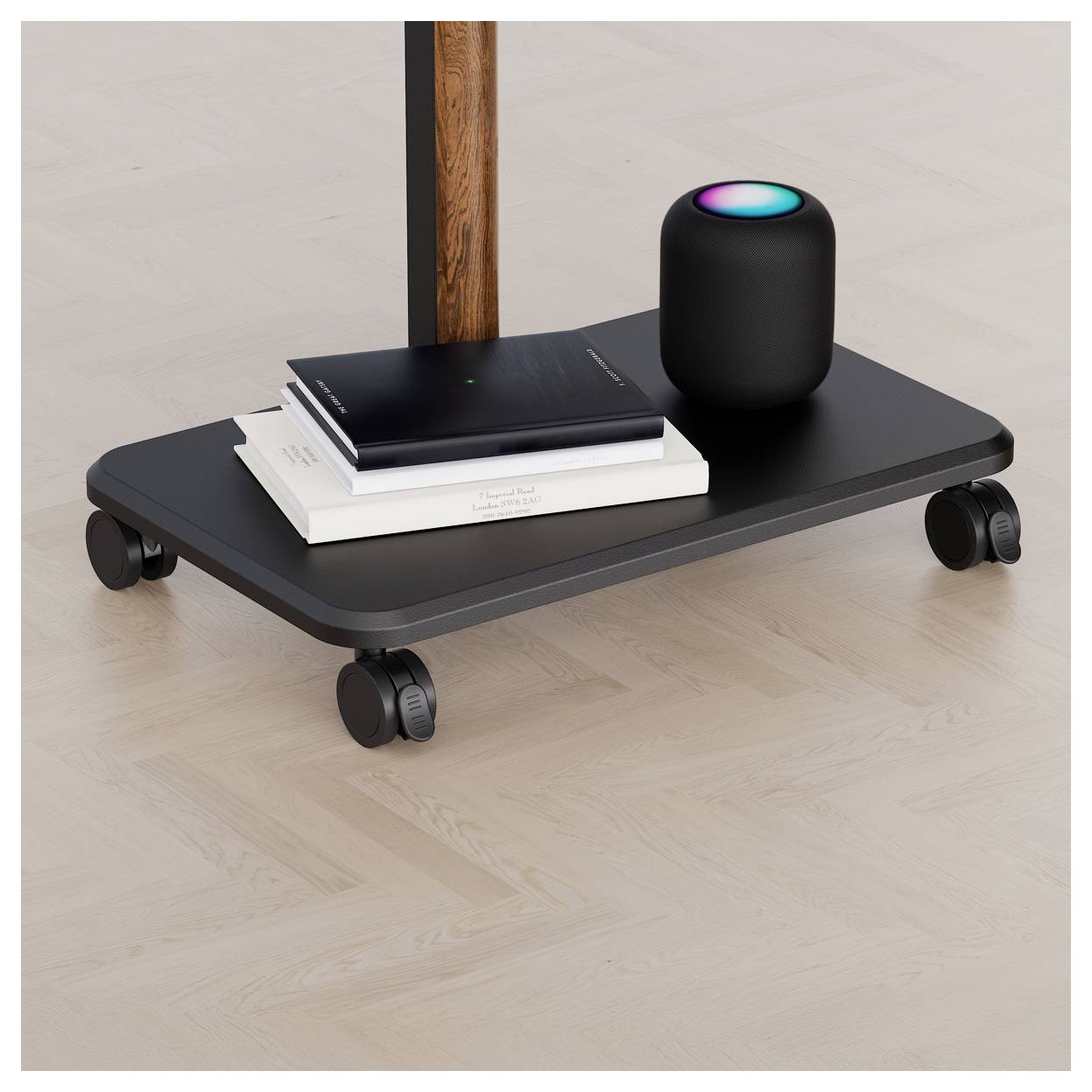 A small black speaker with a glowing top sits on a wheeled shelf beside two stacked books, one with 'The Art of Design' visible.