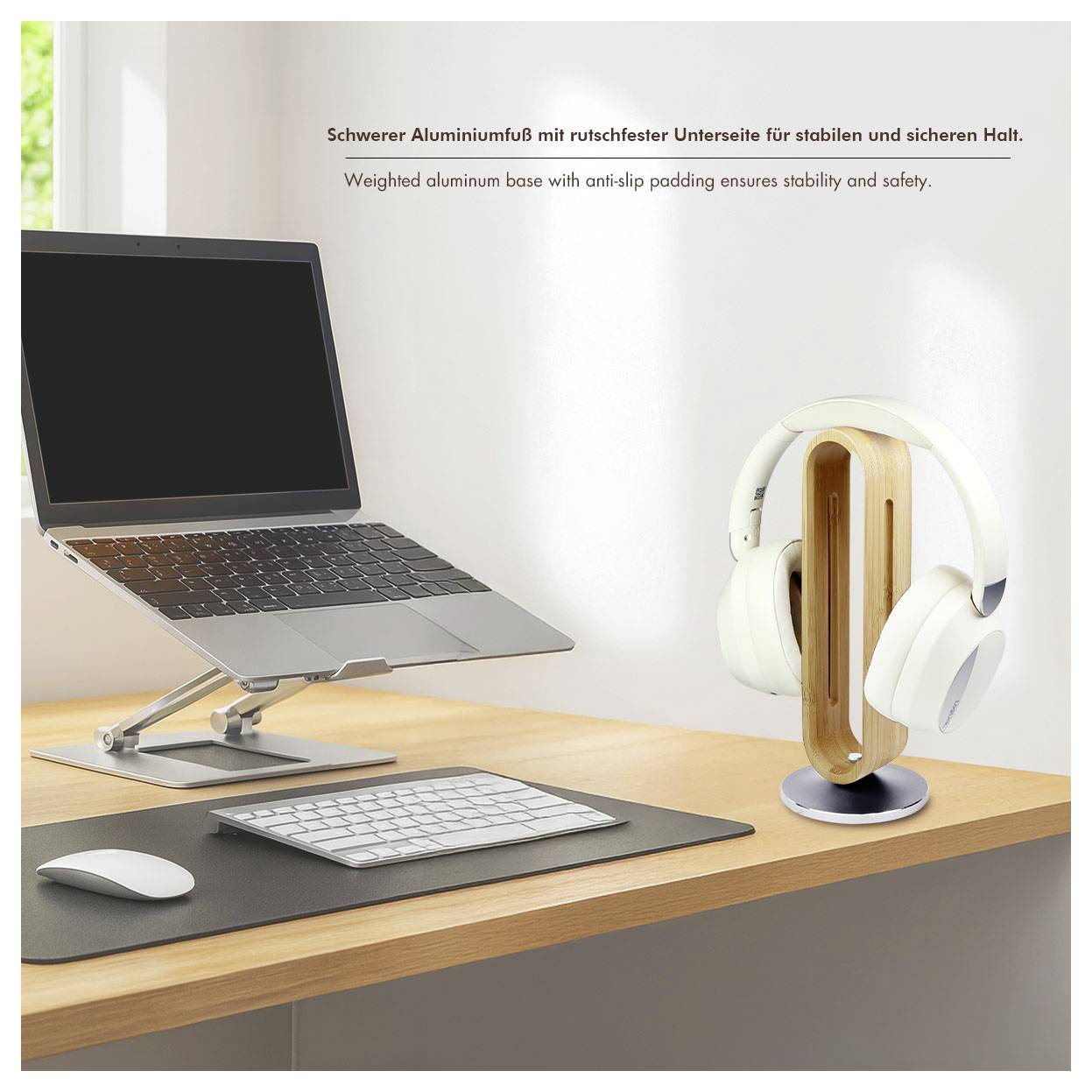 'A laptop on a stand next to a headphone holder with white headphones on a desk. German and English text about the weighted aluminum base.'