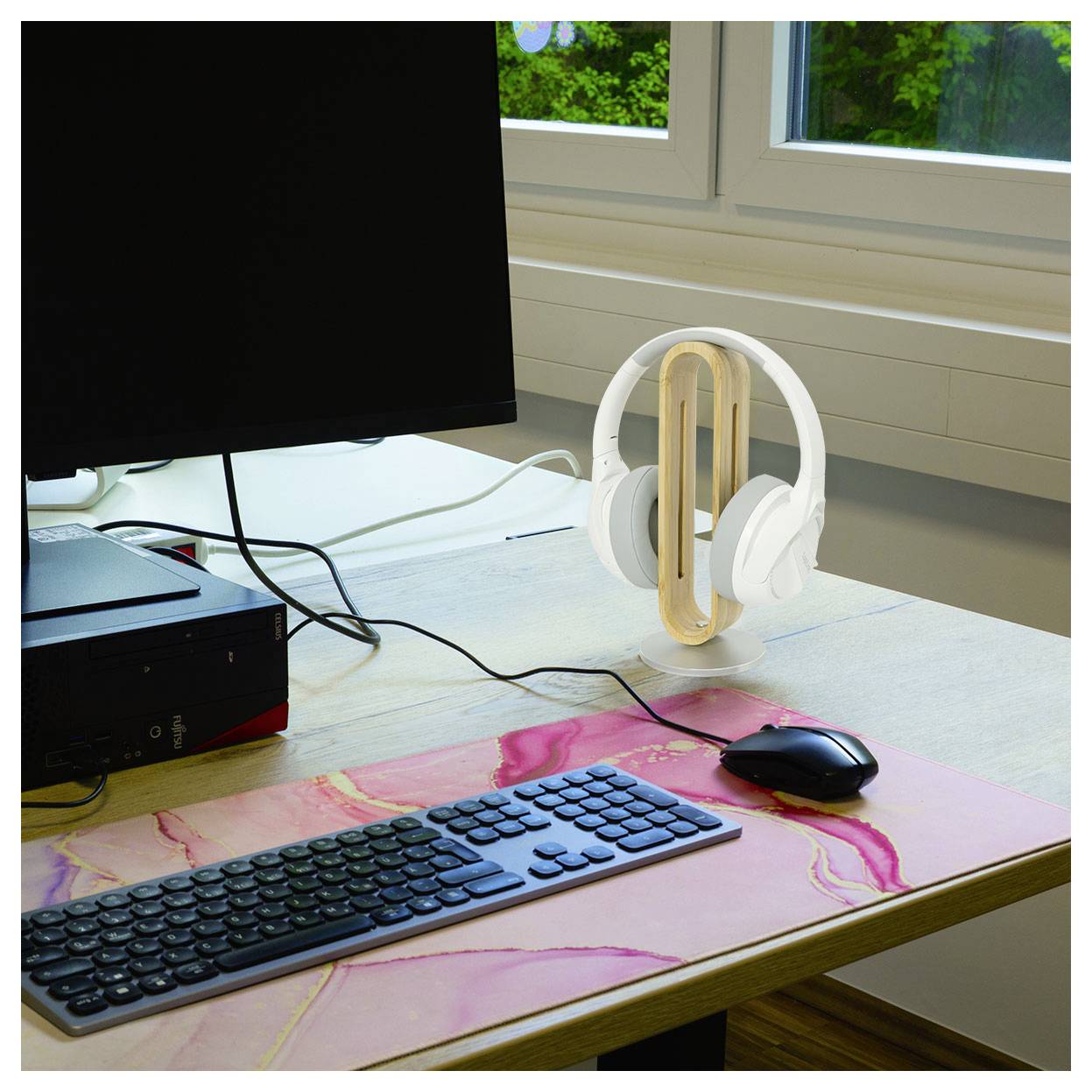 'Modern office desk with a computer monitor, keyboard, mouse, and white headphones stand near a window, creating a tidy workspace.'
