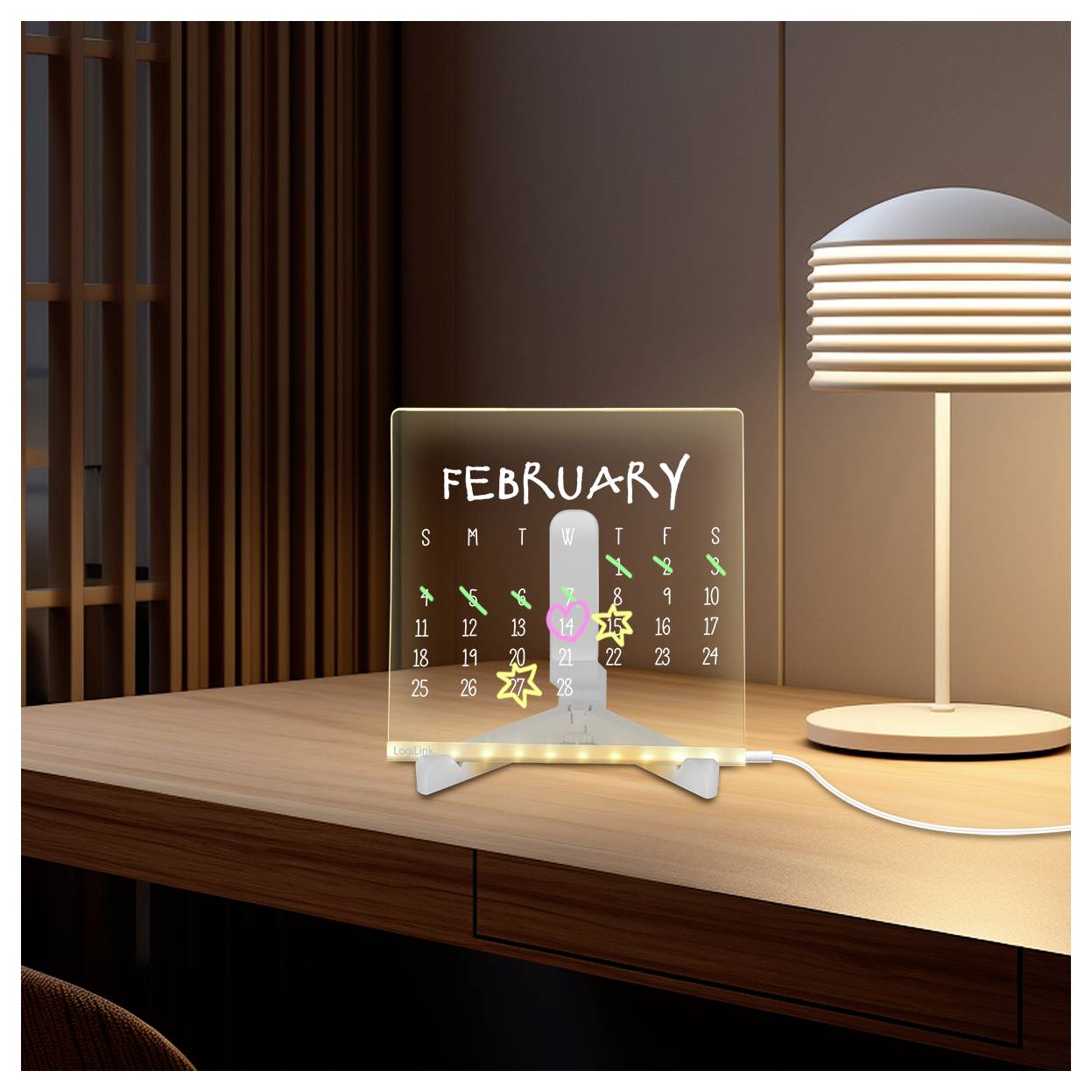 A lit glass calendar showing February on a wooden desk beside a lit table lamp in a modern room.