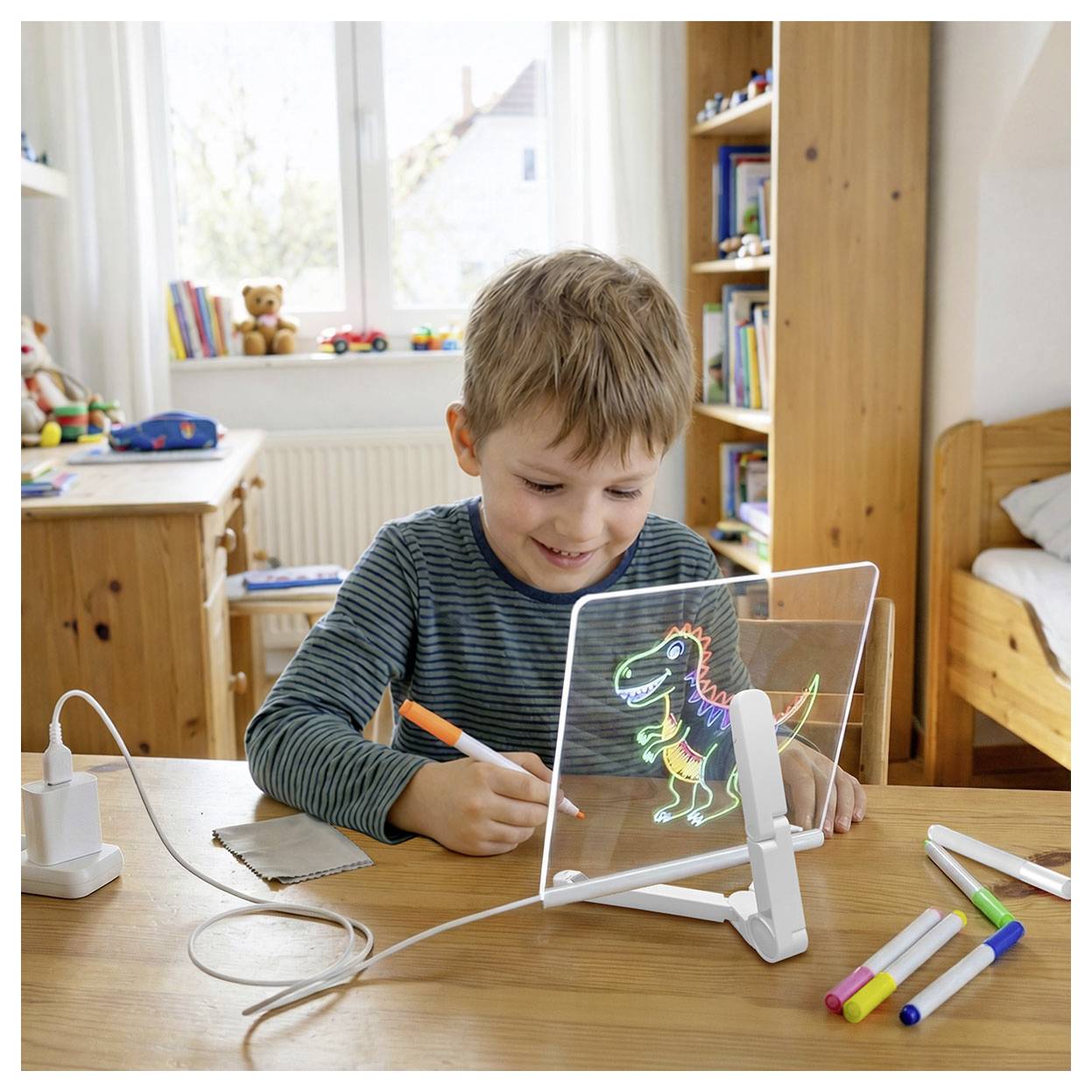 A child draws a dinosaur on a transparent board with colorful markers in a cozy, well-lit room with a desk, bed, and toys.