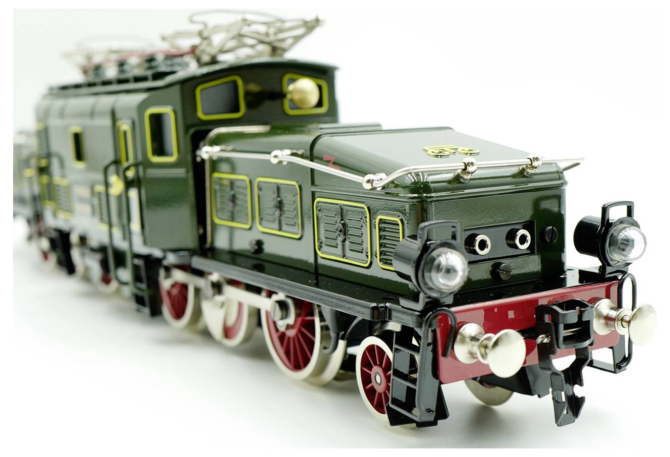 A vintage green toy train model with red wheels and intricate details, viewed from a low angle, showcasing its engine and cab design.